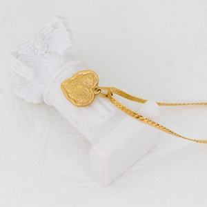 Detail of a textured gold heart pendant resting on a white miniature column prop