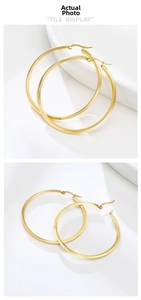 Detailed view of large gold-plated flat hoop earrings on white ceramic tray