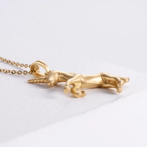 Macro side view of golden matte unicorn pendant necklace laying on white surface