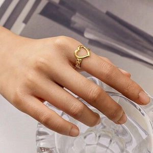 Detail of gold-plated hollow heart ring with chain texture band worn on index finger