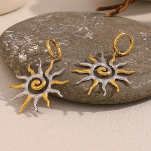 Vue détaillée de boucles d'oreilles soleil bicolores posées sur un galet gris