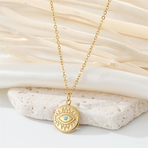 Detail of gold necklace with evil eye pendant and blue stone on white textured stone