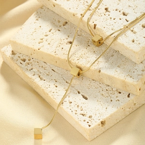Macro shot of gold cube pendant on snake chain over textured beige stone and silk