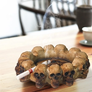 Skull ashtray with vintage design and multiple small skulls on light wood table