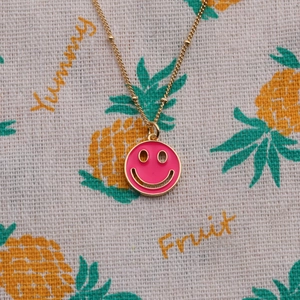 Close-up of pink enamel smiley face pendant with gold plating on a thin cable chain