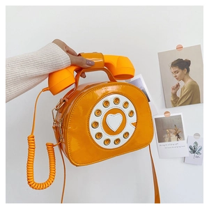 Close-up of creative retro telephone-shaped crossbody bag in bright orange patent leather