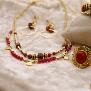 Parure de bijoux multicouches dorée avec perles rouges et gemmes sur tissu blanc