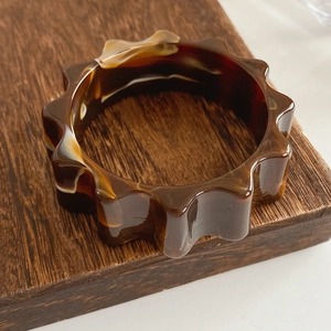 Macro shot of tortoise shell resin bangle with unique wavy gear edges and amber texture