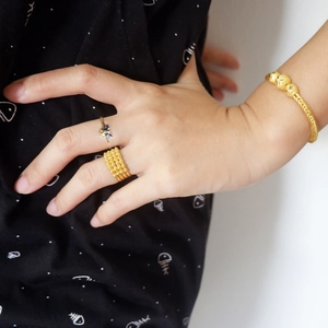 Macro shot of gold weave bracelet, grid band ring, and diamond bee ring set worn on hand