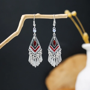 Detail of Bohemian vintage silver fringe earrings with red accents on a wooden branch