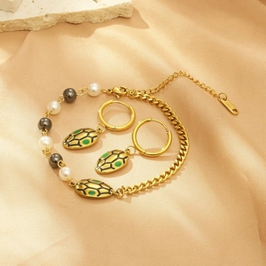 Detailed set of gold snake earrings and pearl bracelet on beige silk fabric