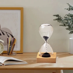 Creative magnetic hourglass with black sand on square wooden base in a cozy office setting