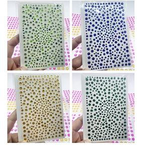 Close-up of four packs of self-adhesive acrylic rhinestone stickers in green, blue, and gold