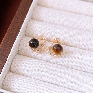 Macro detail of gold-plated gourd stud earrings with tiger eye stone and crystal inlay