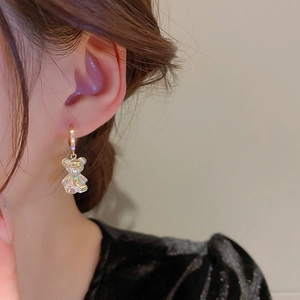 Close-up of a model wearing a gold hoop earring with a colorful crystal teddy bear pendant