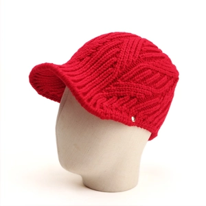 Close-up of red knit peak cap featuring thick textured wool and a round metal buckle detail