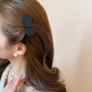 Close-up of a minimalist black circular resin hair clip worn on model's wavy dark hair