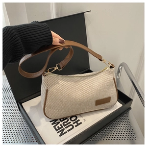 Detail of beige woven fabric underarm bag with brown leather trim and gold hardware