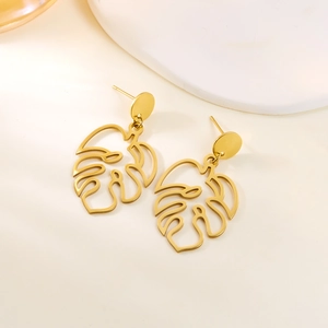 Macro detail of gold-tone hollow monstera leaf earrings with intricate tropical veins