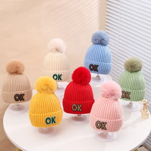 Colorful knitted winter hats for children with OK patches and large fluffy pompoms