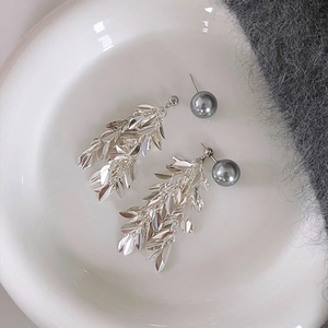 Detailed shot of C-shaped drop earrings featuring grey pearls and silver metallic leaf tassels