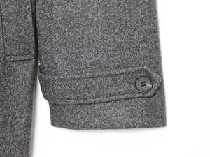 Macro detail of dark grey wool coat sleeve featuring a resin button and textured fabric
