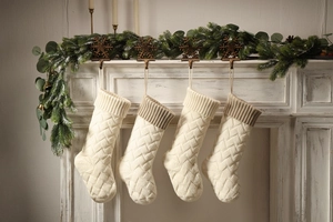Detail of four knit Christmas stockings with cable patterns hanging on a decorated fireplace