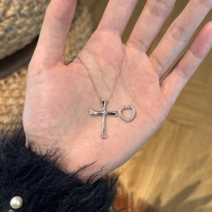 Close-up of S925 sterling silver cross pendant and heart charm held in palm