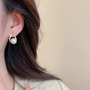 Close-up of golden teardrop earrings with white pearl worn by a model in warm light