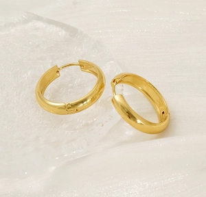 Detailed view of polished 18K gold plated stainless steel hoop earrings on white fabric
