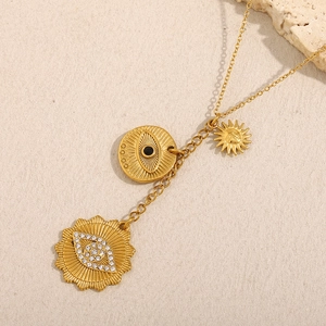 Detail of 18K gold plated evil eye and sun pendants on a textured sand background
