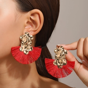 Pendientes de flores doradas con borlas rojas en forma de abanico usados por el modelo
