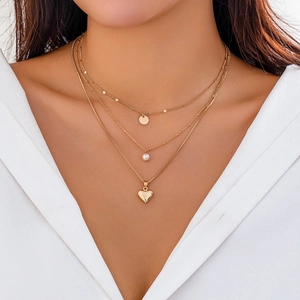 Detail of three-layer gold necklace featuring round disc, pearl, and heart pendants on model