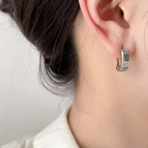 Close-up of polished two-tone curved hoop earring worn on ear with gold and silver finish