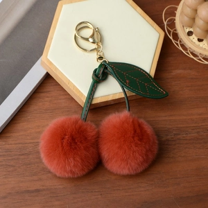 Detail of red faux rabbit fur cherry keychain with green leaves on wooden background