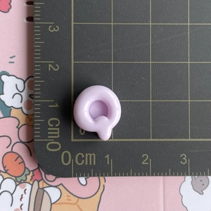 Close-up of small purple resin letter 'a' hair clip accessory with measuring ruler