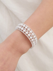 Detail view of a four-layer rhinestone and pearl bracelet worn on a model's wrist