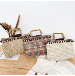 Close-up of straw beach tote bags with gold D-shaped handles and brown pom-pom charms