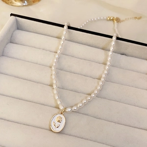 Détail d'un collier de perles avec pendentif rose dorée sur émail blanc