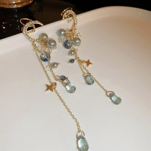 Détails de boucles d'oreilles luxe avec étoile, lune et cristaux bleus sur plateau blanc