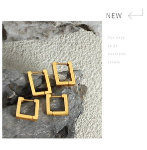 Macro shot of gold-plated rectangular geometric hoop earrings on a grey stone background