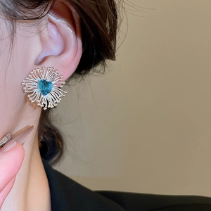 Gros plan d'une boucle d'oreille cœur avec pierre bleue et cadre radial argenté sur l'oreille