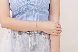 Close-up of gold chain bracelet with sparkling diamond letter L pendant on wrist