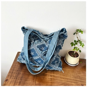 Detail of vintage denim tote bag featuring frayed edges and star print on wooden table