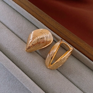 Macro shot of gold shell-shaped hoop earrings with vertical ribbed metal texture