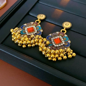 Détail de boucles d'oreilles bohèmes avec pierres rouges, émail et pompons en perles dorées