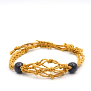 Detail of handmade yellow woven cord bracelet featuring an intricate mesh pattern and black beads