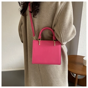 Close-up of vibrant pink crossbody bag styled with a beige wool coat for a chic look