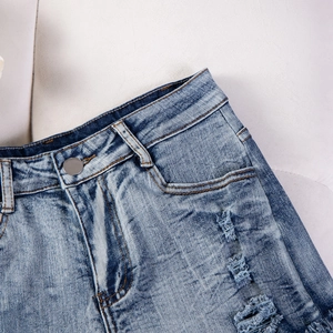 Vista dettagliata di pantaloncini di denim azzurro con texture strappata e bottone in metallo