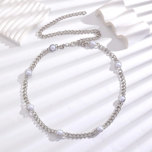 Detail of silver chain belt with round white pearls on a textured white background